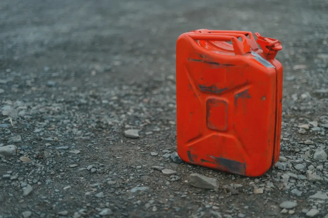 How to Dispose of Old Gasoline : Old red metal gasoline can sitting on gravel