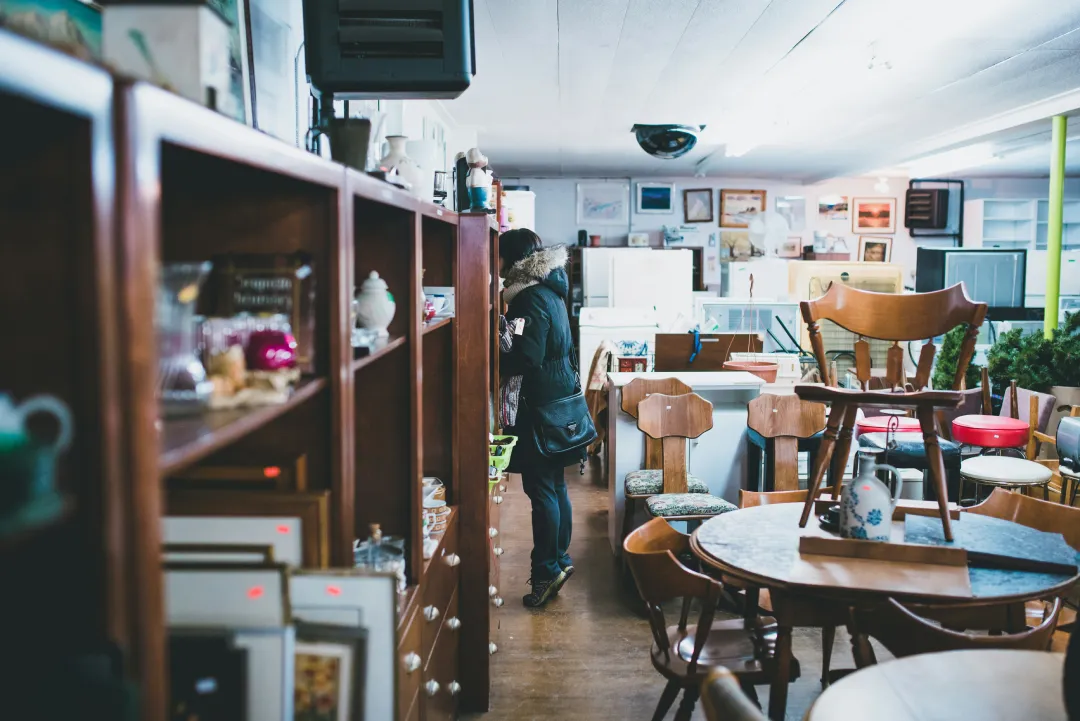 Shopper browsing donated chairs, tables and housewares in a secondhand thrift store