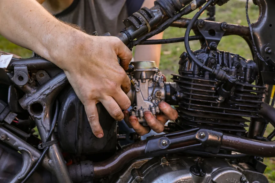 Hands removing a carburetor from a small engine clogged by old gasoline