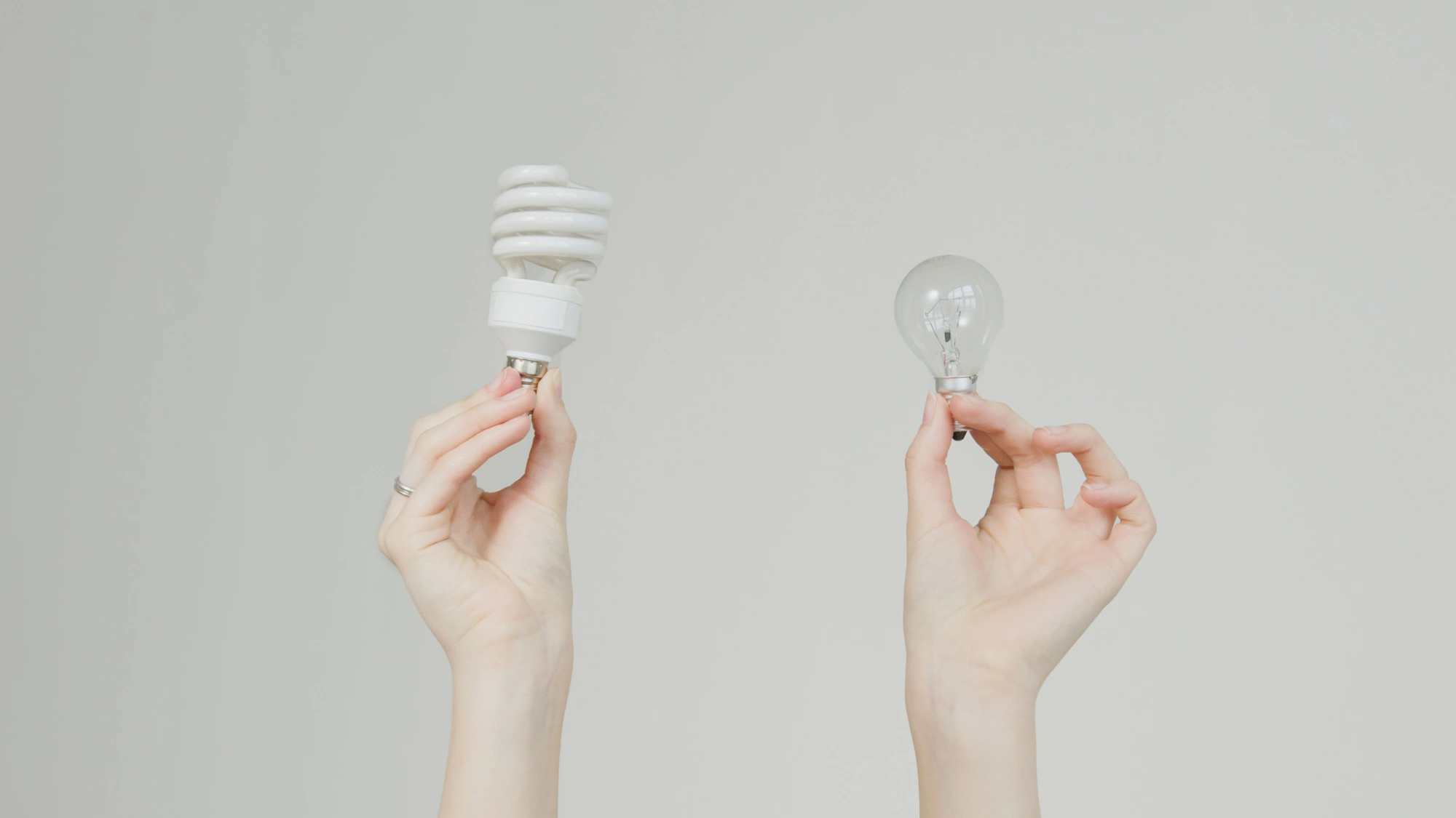 Hands holding a spiral CFL and an incandescent bulb, the distinction that decides recycling tube fluorescents and CFLs