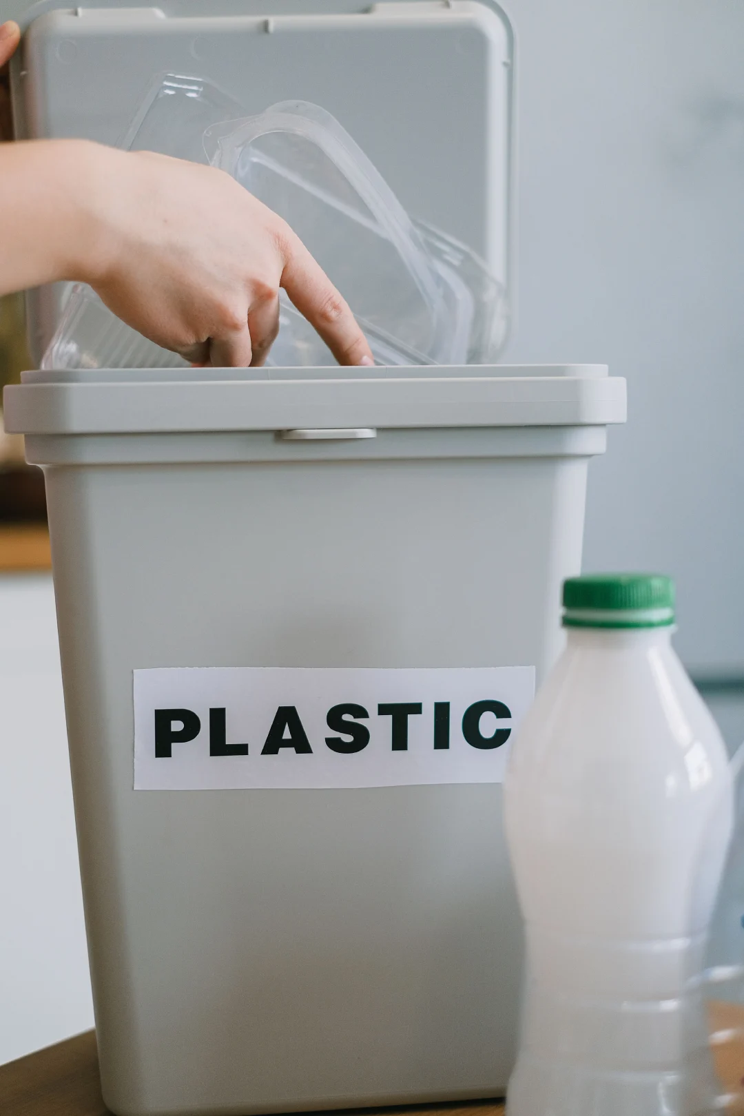 Indoor Plastic Sorting Bin A hand dropping clear plastic containers into a kitchen bin labeled PLASTIC